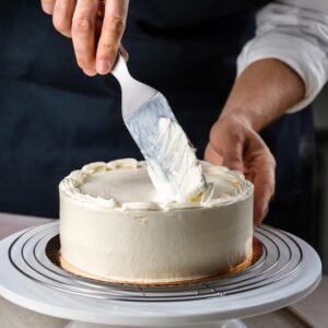 A baker frosting a cake with white buttercream