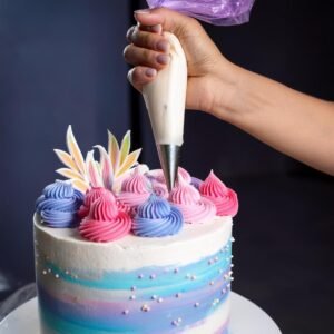 A baker piping colorful buttercream rosettes onto a cake.