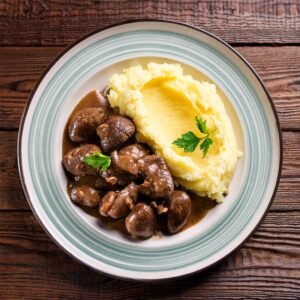 A plated dish of braised chicken hearts served with mashed potatoes and fresh herbs