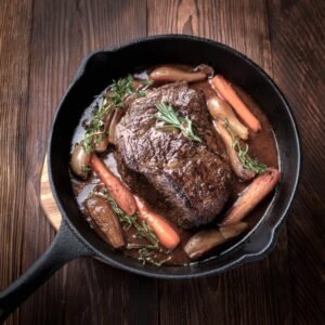 Chuck eye steak braising in a skillet with vegetables