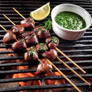 Chicken hearts on skewers, grilled over an open flame, served with chimichurri sauce