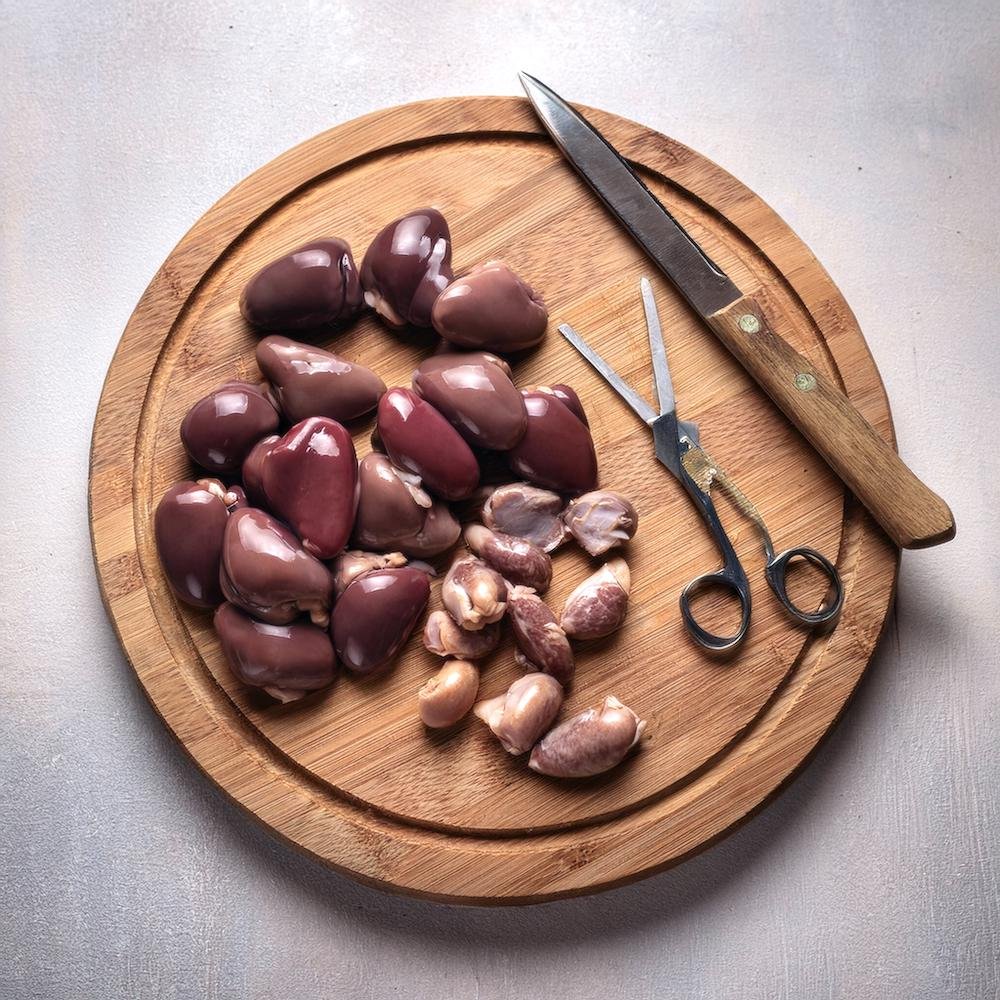 Chicken hearts and gizzards displayed side by side on a wooden cutting board