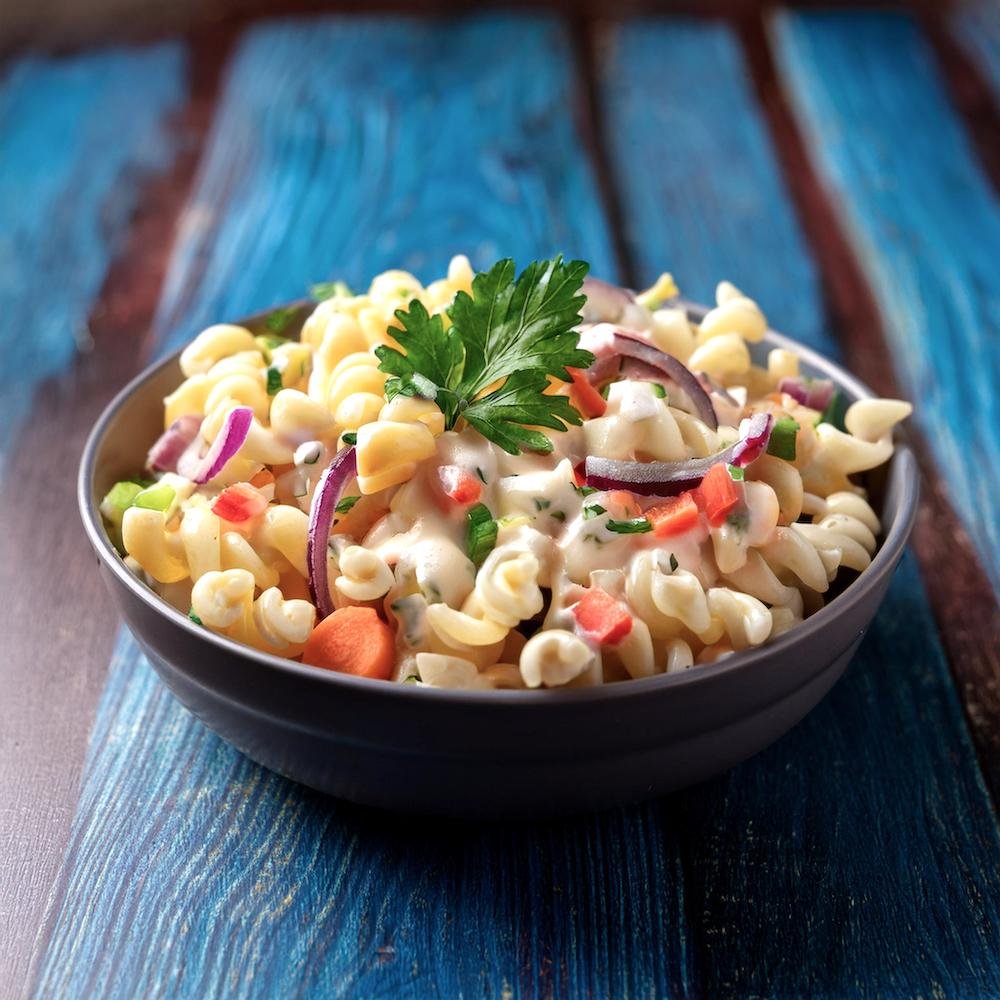 A bowl of macaroni salad with fresh vegetables and creamy dressing, garnished with parsley