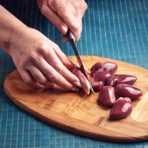 Raw chicken hearts being trimmed and cleaned on a wooden cutting board