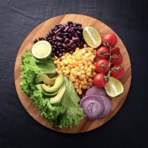 Fresh vegetables, avocado, and beans laid out on a wooden cutting board