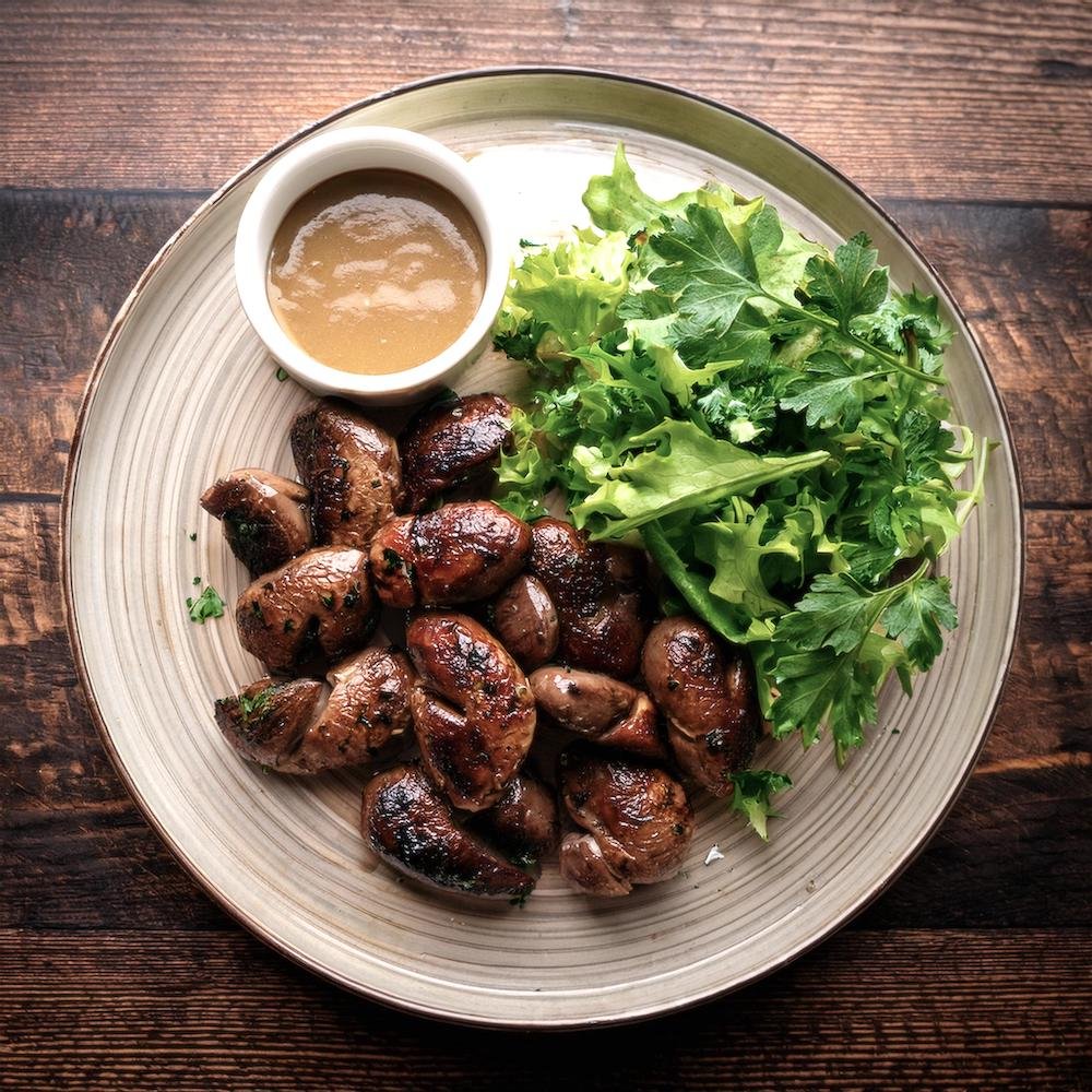 A plate of grilled chicken hearts served with a fresh salad and dipping sauce