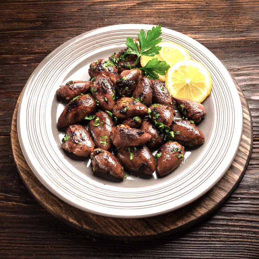 A platter of grilled chicken hearts garnished with fresh herbs and lemon wedges