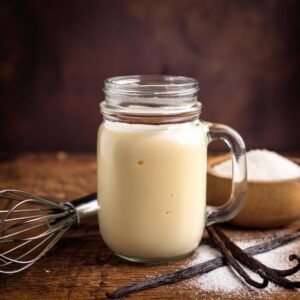 Homemade sweet cooking cream in a glass jar, surrounded by sugar and vanilla pods