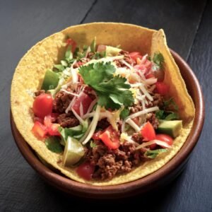 A taco salad served in a tortilla bowl with ground beef and colorful toppings