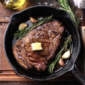 A cast-iron skillet with a seared chuck eye steak and melted herb butter