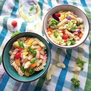 Two bowls, one with pasta salad and the other with macaroni salad, displayed on a checkered tablecloth