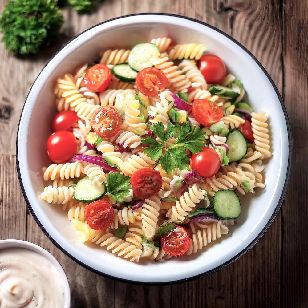 A colorful pasta salad in a white bowl, garnished with fresh herbs and vegetables. Title: Perfectly Made Pasta Salad