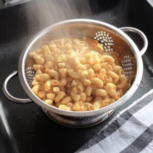 Elbow macaroni being drained in a colander after cooking