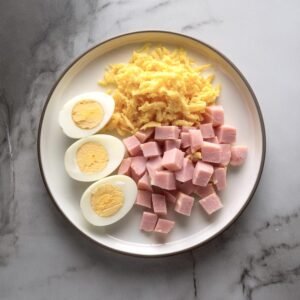 A plate with cubed ham, hard-boiled eggs, and shredded cheese