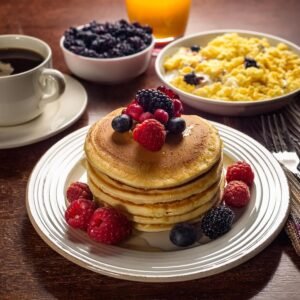 Sweet cream pancakes served with fresh fruit, scrambled eggs, and coffee