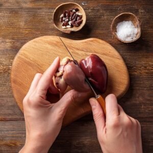 Hands trimming chicken hearts with a knife on a cutting board