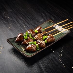 A serving of yakitori-style chicken hearts garnished with green onions and sesame seeds