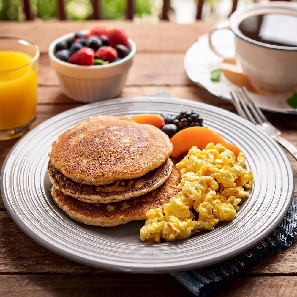 A balanced breakfast plate with two pancakes, scrambled eggs, and fresh fruit.