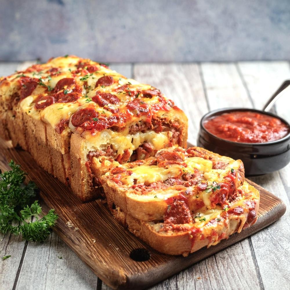 Sliced garbage bread filled with pepperoni, cheese, and marinara sauce, served on a wooden board.