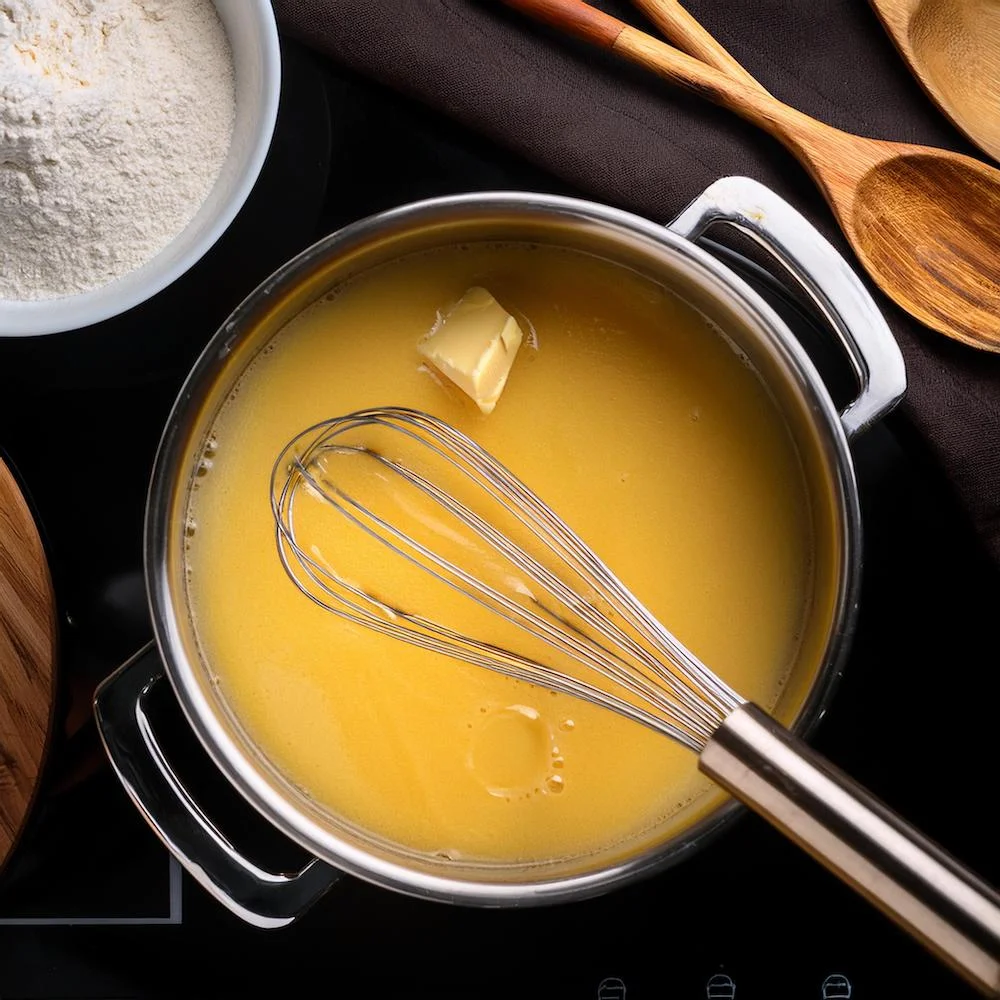 Butter and flour being whisked together in a saucepan to create roux.