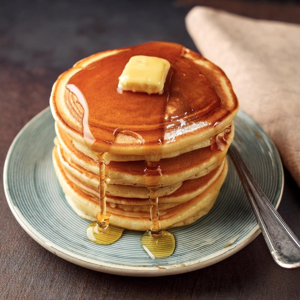 A close-up of fluffy pancakes with syrup dripping down the sides