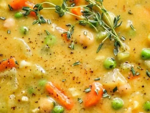 Bowl of creamy vegetable soup with colorful vegetables, garnished with herbs.