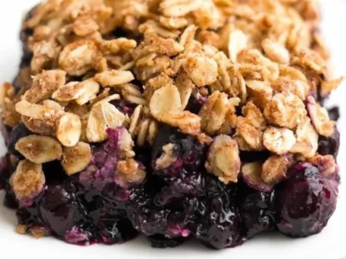 A healthy blueberry crumble served in a bowl, topped with oats and fresh blueberries.