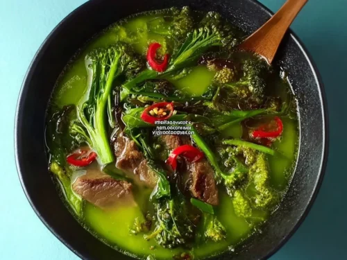 Bowl of herb and coconut broth with noodles, garnished with fresh herbs