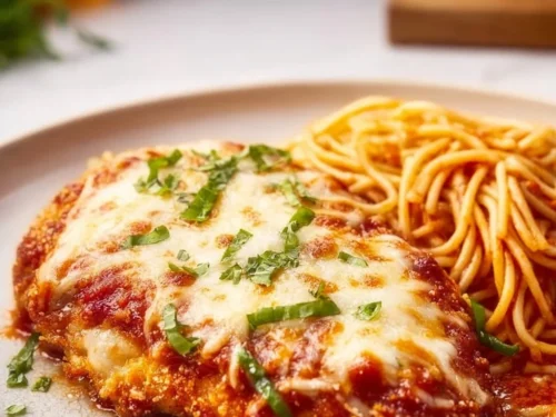 Baked Chicken Parmesan on a plate with cheese and herbs garnish